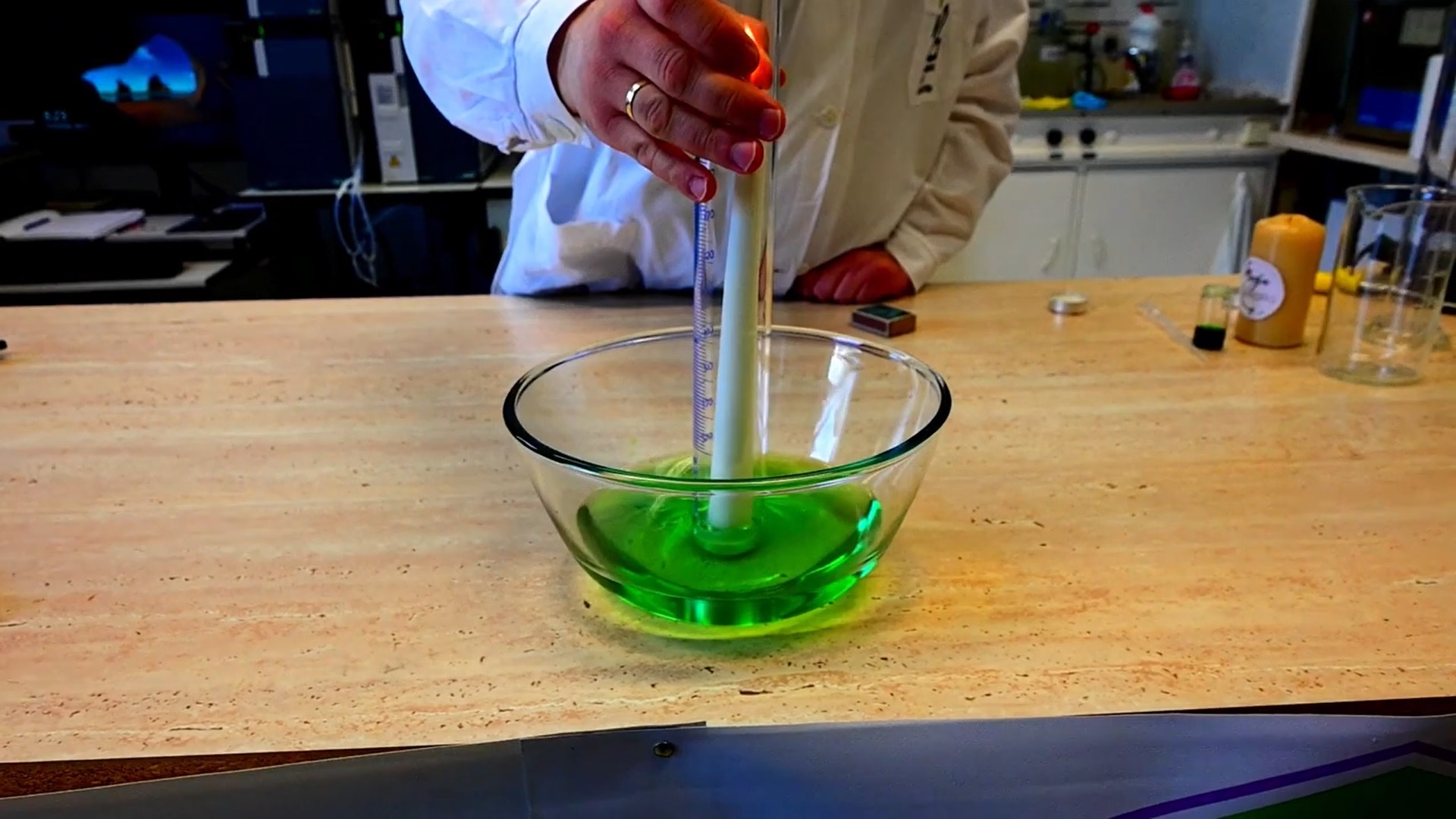 Miska z zielonym płynem i płonącą świeczką przykryta cylindrem miarowym